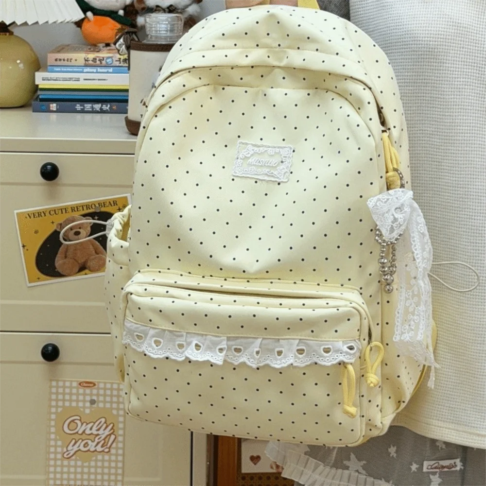 A cream-colored polka dot nylon travel backpack with a laptop compartment and lace trim.