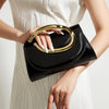 A woman holds a black leather clutch purse with a gold handle against a light-colored dress.