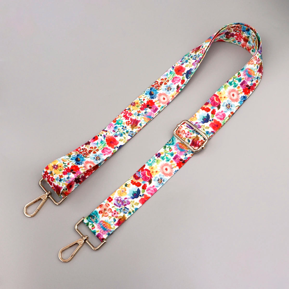 A floral patterned fabric strap with a gold buckle is shown against a gray background.