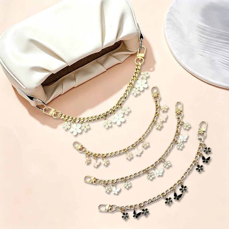 Gold chain necklace with white flower and leaf charms displayed next to a cream-colored bag.