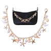 A gold-toned bohemian layered chain necklace with starfish and pearl charms displayed next to a black leather pouch.