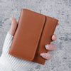 A hand holds a brown leather slim multi-functional card wallet against a gray background.