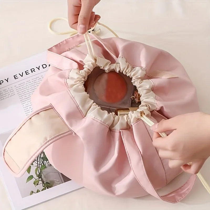 A pink satin makeup organizer bag with a decorative opening is being held by a hand.