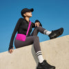 A woman wearing a black top and gray leggings leans against a concrete wall under a blue sky.