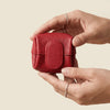 A hand holds a small, red leather coin purse with a snap closure.