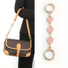 A brown leather handbag with a gold chain shoulder strap and a pink heart pendant.