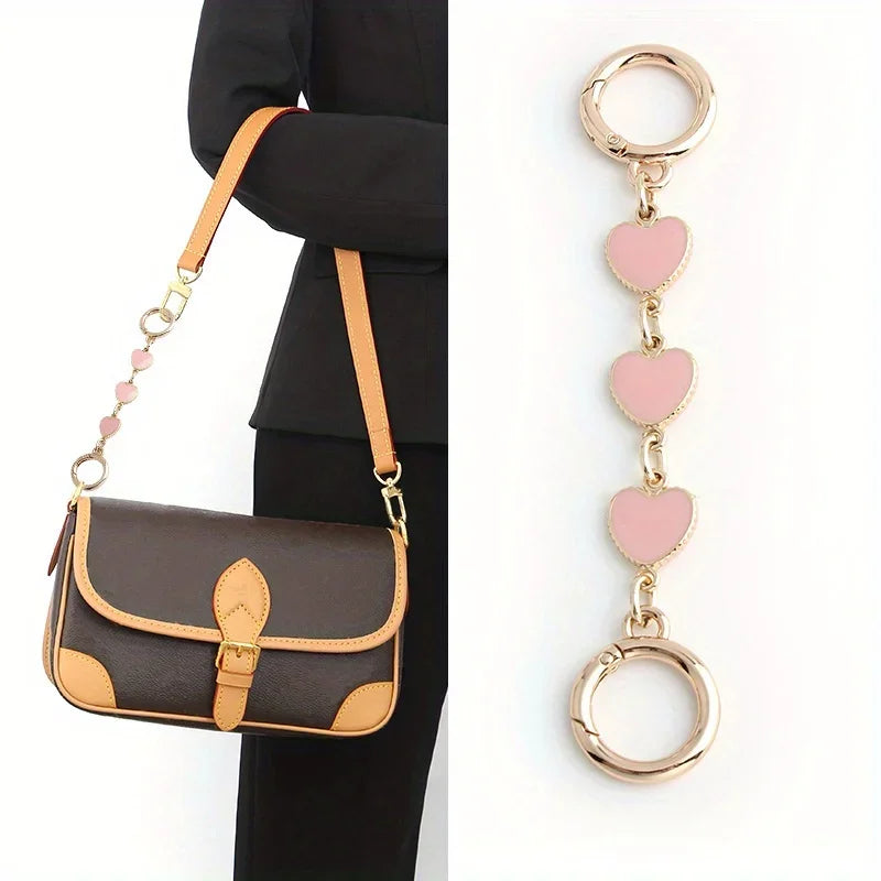 A brown leather handbag with a gold chain shoulder strap and a pink heart pendant.