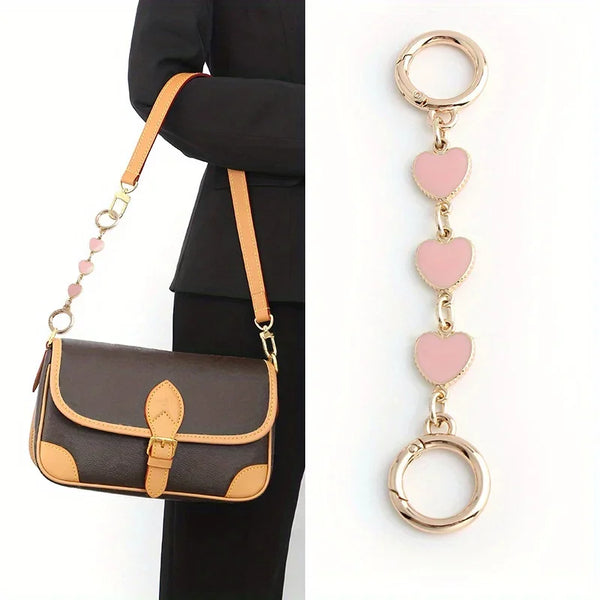 A brown leather handbag with a gold chain shoulder strap and a pink heart pendant.