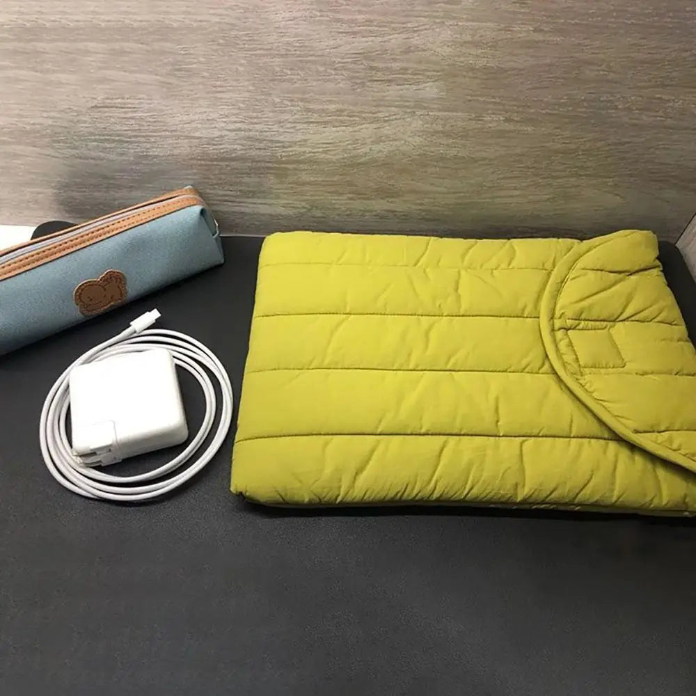A yellow quilted laptop sleeve is shown next to a white charging cable and a light blue leather pouch.