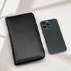 A black leather wallet and a matching smartphone are shown on a light surface.