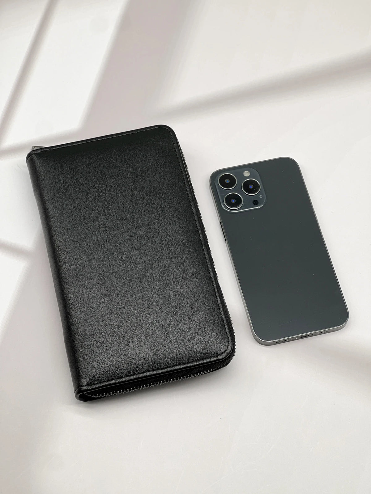 A black leather wallet and a matching smartphone are shown on a light surface.