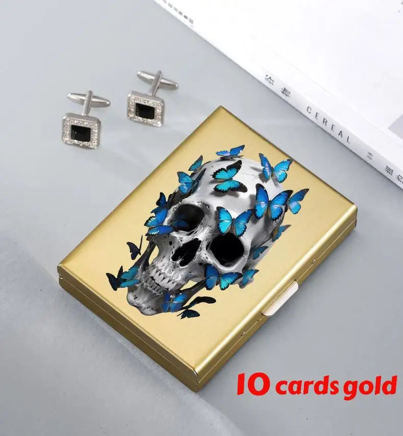 A gold card holder featuring a skull design with blue butterfly accents and small silver earrings.