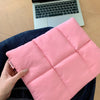 A pink quilted laptop sleeve is being held by a hand, resting on a dark blue shirt.