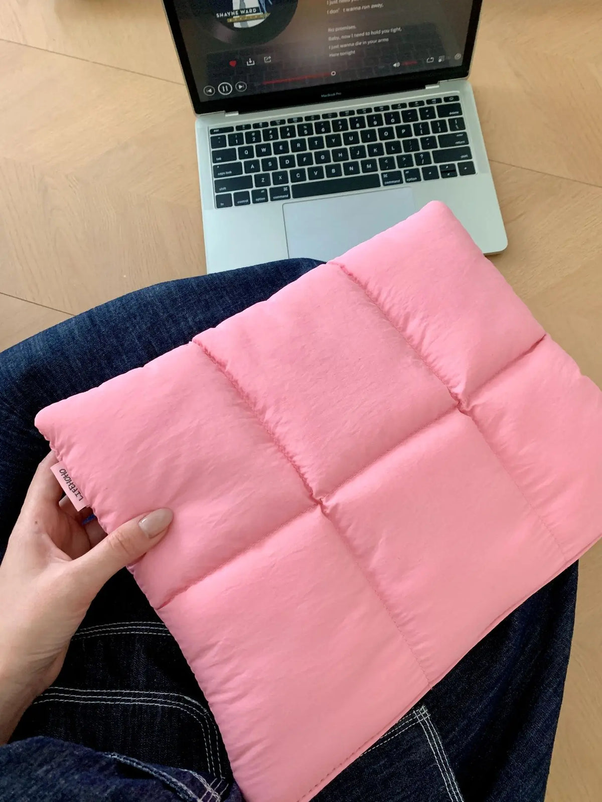 A pink quilted laptop sleeve is being held by a hand, resting on a dark blue shirt.