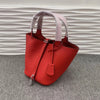 Helles orange-rotes Leder-Eimertasche mit hellrosa Stoffgriffen auf grauem Untergrund.