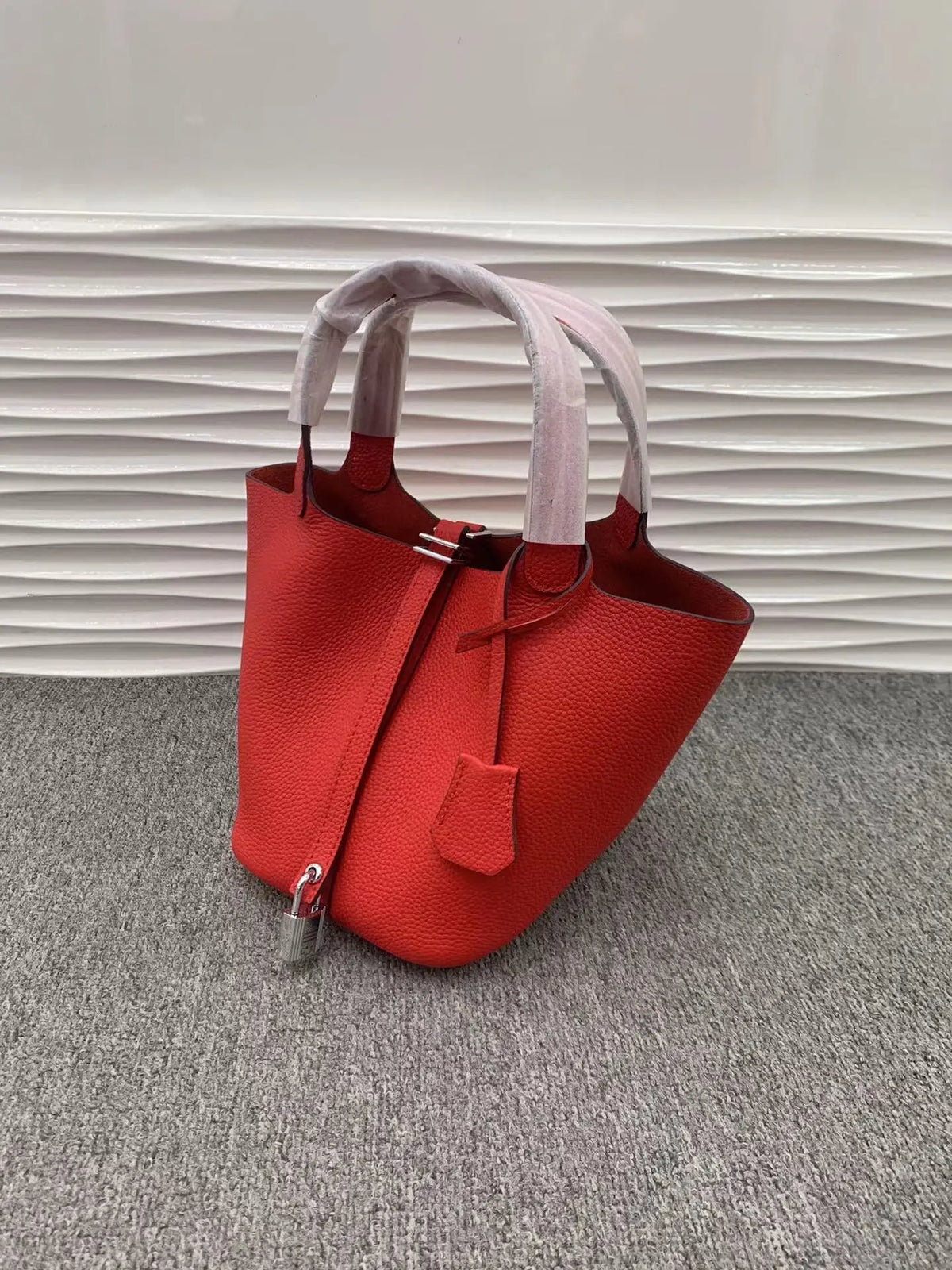Helles orange-rotes Leder-Eimertasche mit hellrosa Stoffgriffen auf grauem Untergrund.
