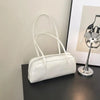 A white glossy PU leather tote bag with dual straps resting on a dark surface next to a silver lamp.
