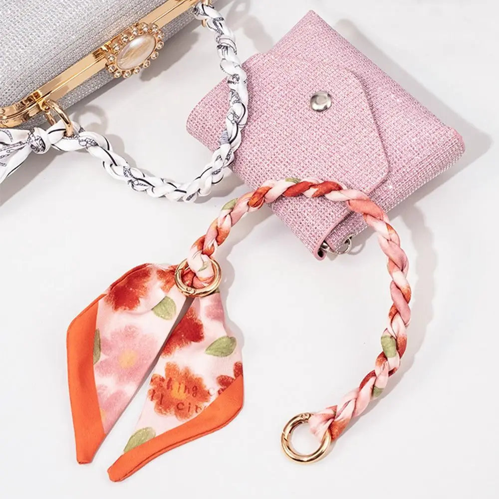 Rosa Seideschal-Taschenkette mit goldener Schnalle und orangefarbigem Blumenetikett vor weißem Hintergrund