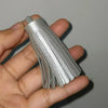 A hand holds a set of silver leather tassel fringe craft supplies.