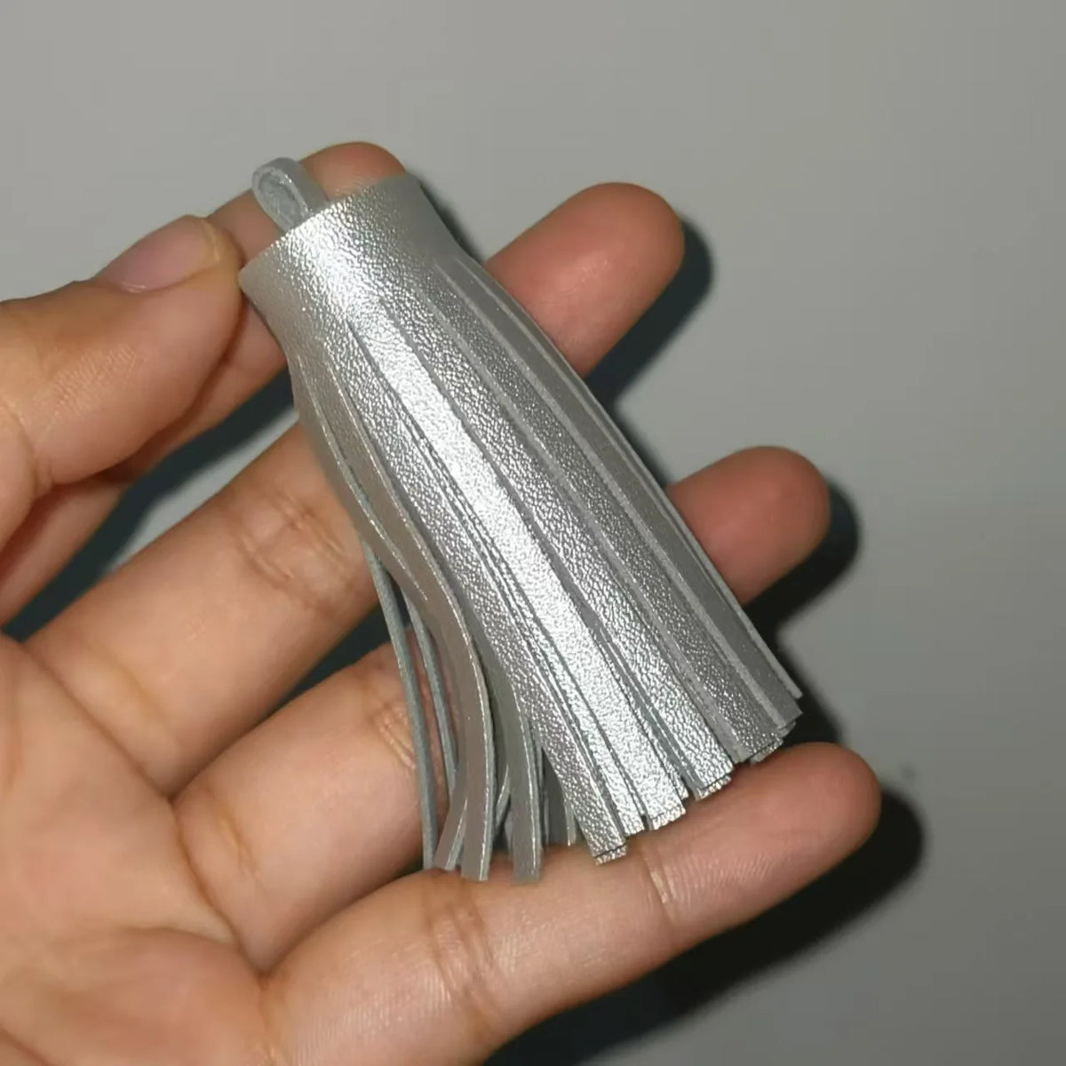 A hand holds a set of silver leather tassel fringe craft supplies.