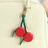 A red cherry fruit shape coin purse keychain attached to a light cream leather handbag.