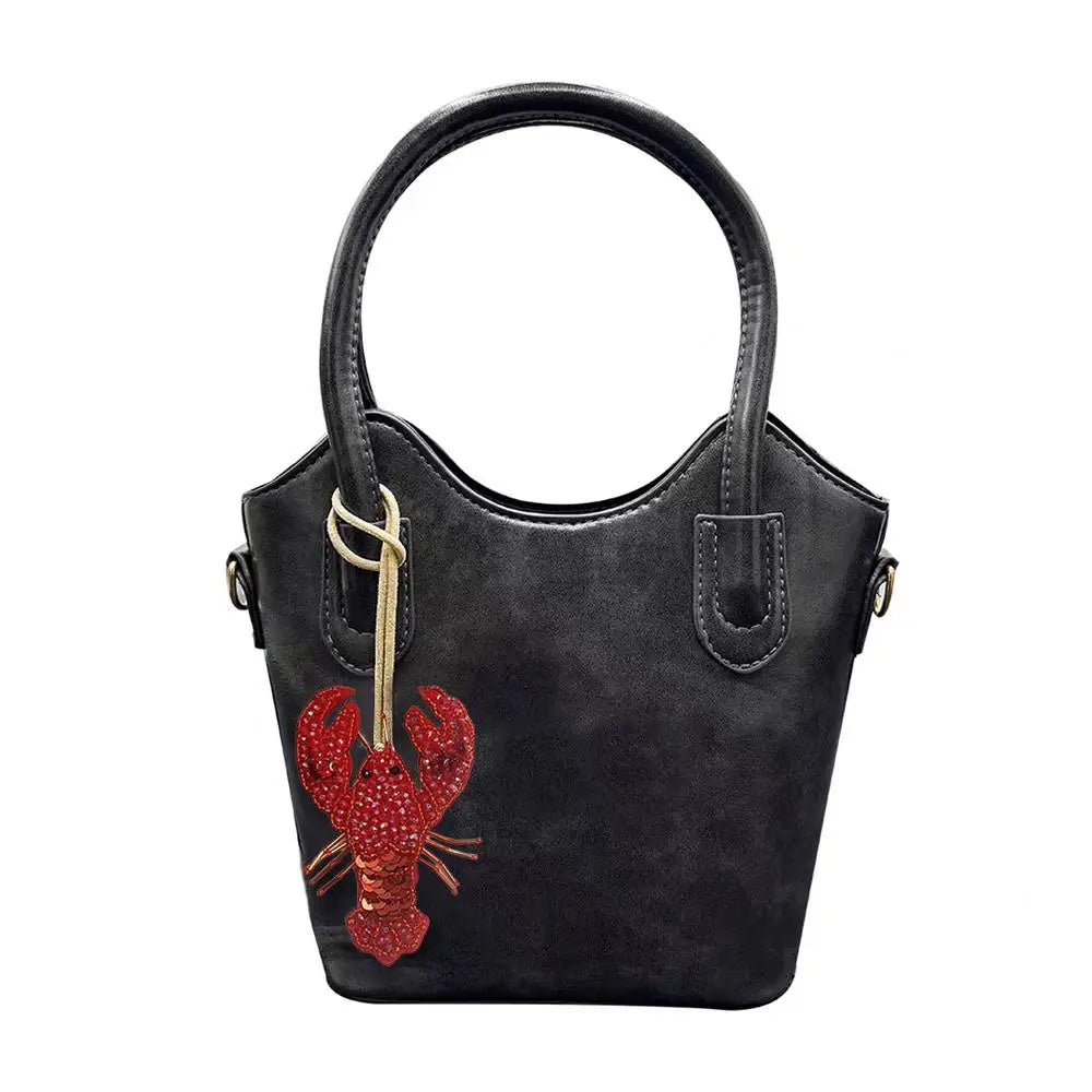 A black handbag with a handle featuring a red crab charm made of rhinestones.