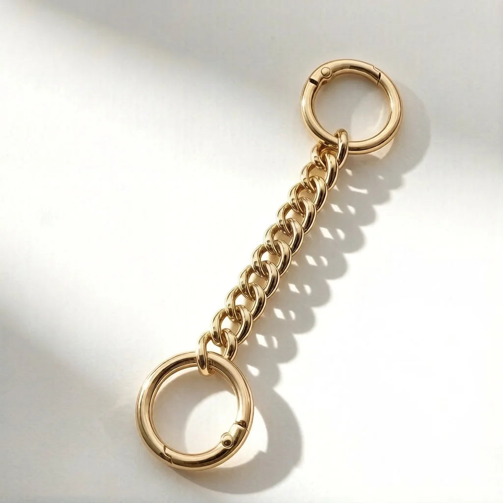 A gold-toned metal chain extender with a circular loop, shown against a white background.