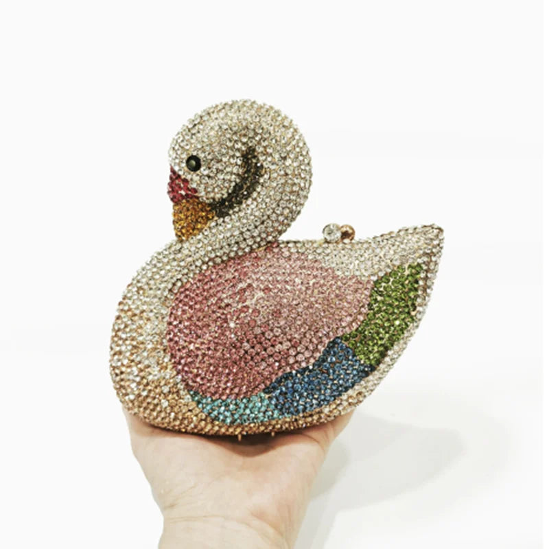 Une main tient un sac à main soirée en cristal de cygne recouvert de pierres roses et vertes scintillantes.