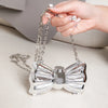 A hand holds a silver heart-shaped acrylic clutch with a chain strap against a light background.