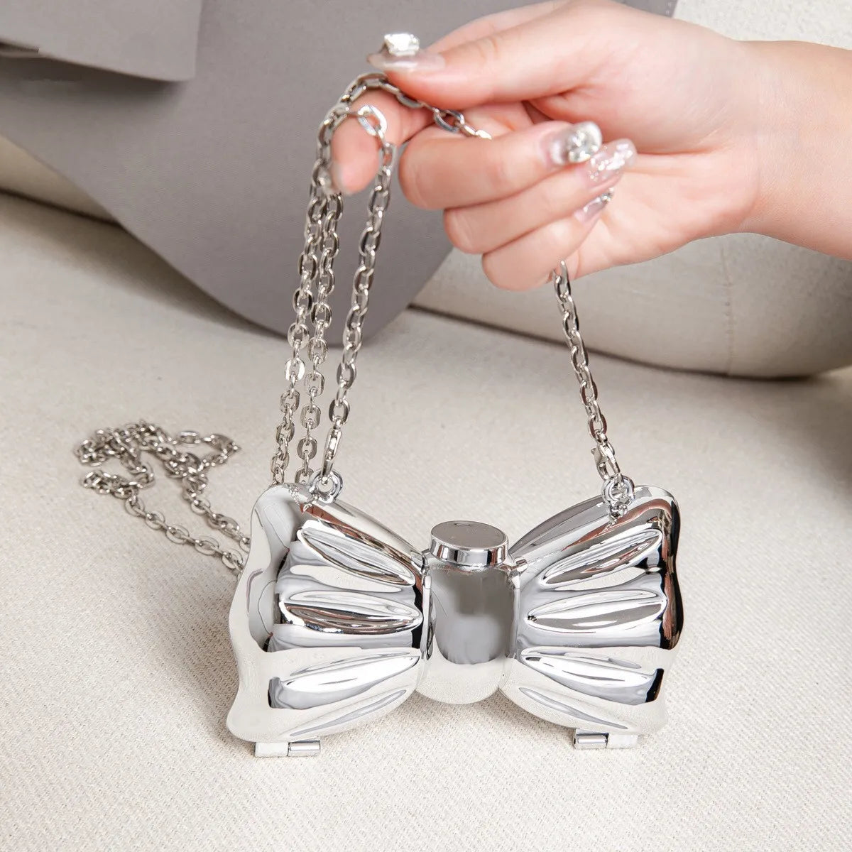 A hand holds a silver heart-shaped acrylic clutch with a chain strap against a light background.