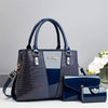 Bolso y cartera de cuero de cocodrilo patentado azul marino sobre una superficie blanca.
