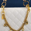 Gold chain necklace with a cherry flower pendant draped over a white quilted leather bag.