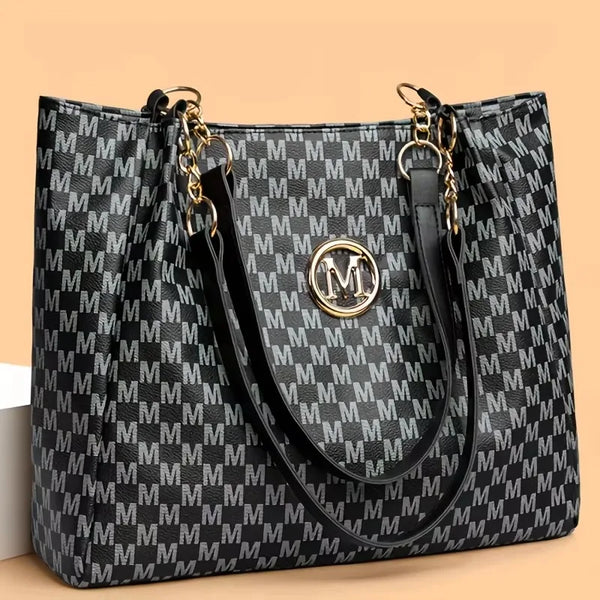A black and white geometric monogram print tote bag with gold hardware shown from the front.