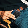 A hand is inserting an RFID blocking card into the front pocket of blue jeans.