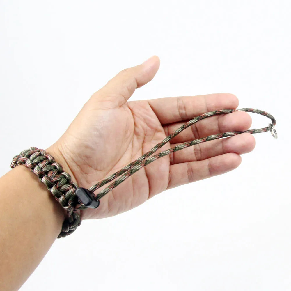 A hand is holding a handwoven paracord camera wrist strap with a dark green and brown pattern.