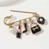 Gold-toned alloy brooch pin featuring black and white accents, including pearl and glitter details.