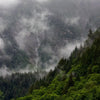 Nebelverhangenes Bergpanorama mit Wasserfall, der über steile bewaldete Hänge stürzt