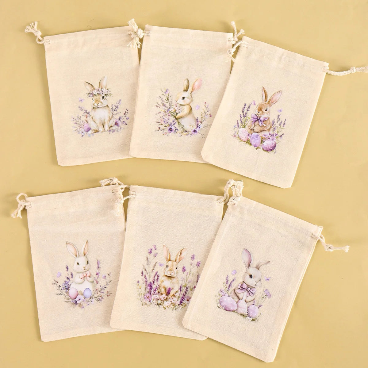 A set of six natural linen drawstring gift bags featuring delicate illustrations of rabbits and purple flowers.
