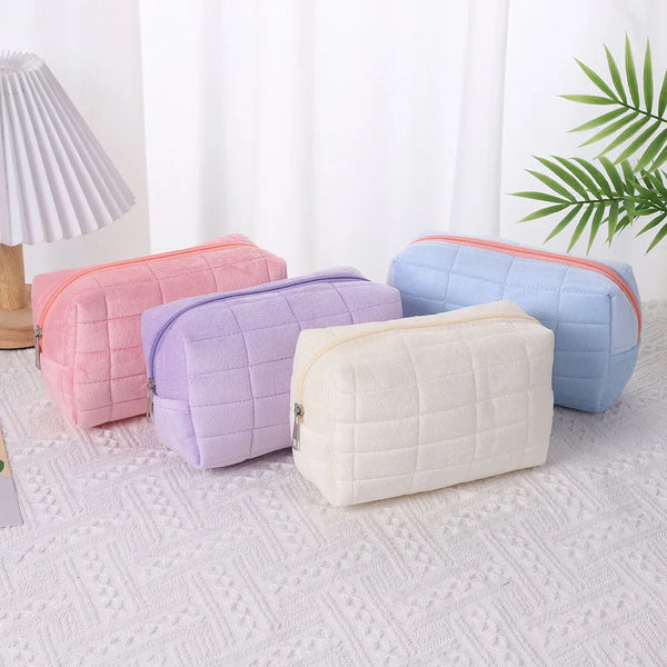 A collection of pastel quilted velvet cosmetic and toiletry bags in pink, lavender, blue, and cream colors.