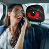 A woman in a blue jacket is looking at her phone while sitting in a car, with a black and red eye design on the headrest.