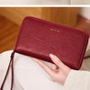 A close-up of a deep red leather wallet with a zipper closure and a leather strap, held by a hand.