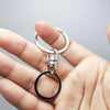 A hand holds a silver swivel keychain hook with a secure clasp.