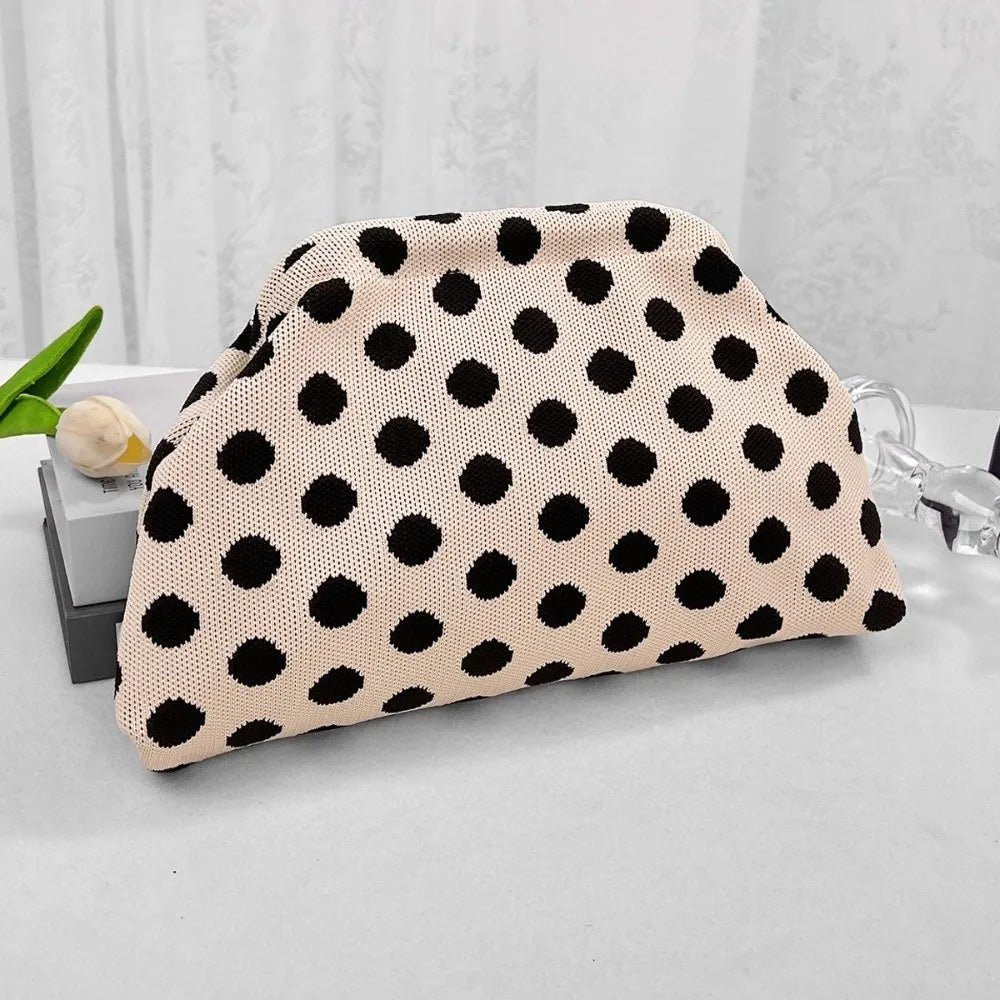 A beige clutch bag with black polka dots resting on a white surface.