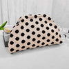 A beige clutch bag with black polka dots resting on a white surface.