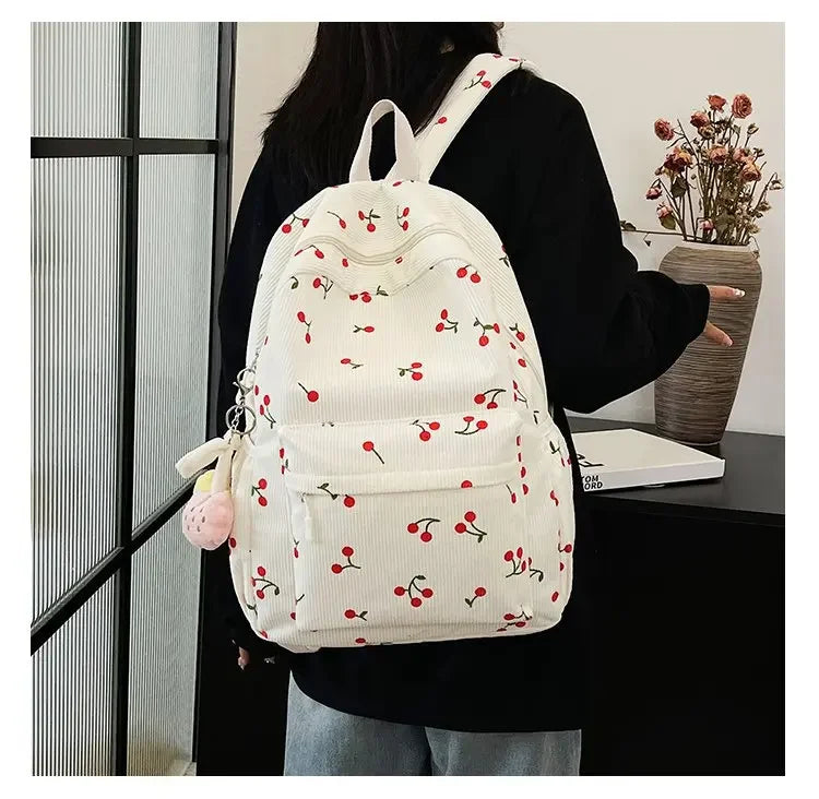 A white corduroy fashion backpack with a floral pattern and adjustable strap is worn by a person.