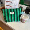 Una bolsa de lienzo con rayas verdes y negras junto a una taza de café helado.