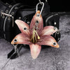 A realistic orchid flower keychain with pink and white petals attached to a black leather bag.