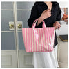 A pink and white striped waterproof PVC shoulder tote bag is held by a person in front of a glass door.
