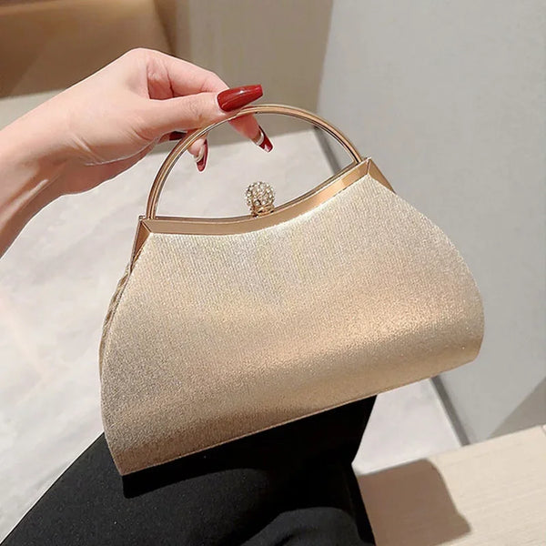 A hand holds a beige pleated glitter evening handbag with a top handle and chain strap.