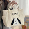A beige canvas shoulder bag featuring a Snoopy cartoon design, held by a person.